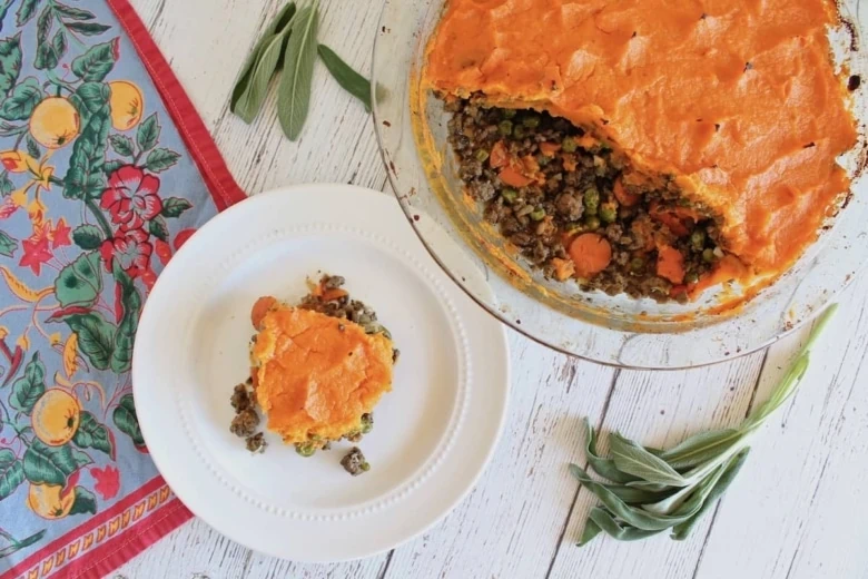 overhead view of sweet potato shepherd's pie with pieces taken out of it and a slice on a separate white plate