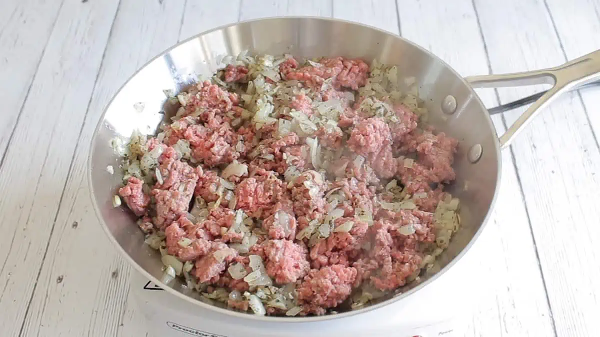 Onions and ground beef cooking in a stainless steel pan