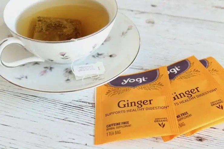 Individually wrapped ginger tea bags next to a tea cup and saucer with tea in it
