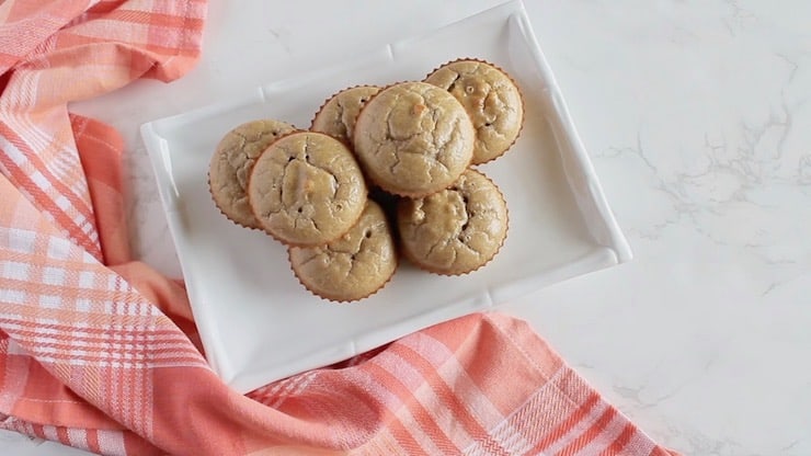 Overhead view of six applesauce muffins on a white plate next to a red and white plaid napkin