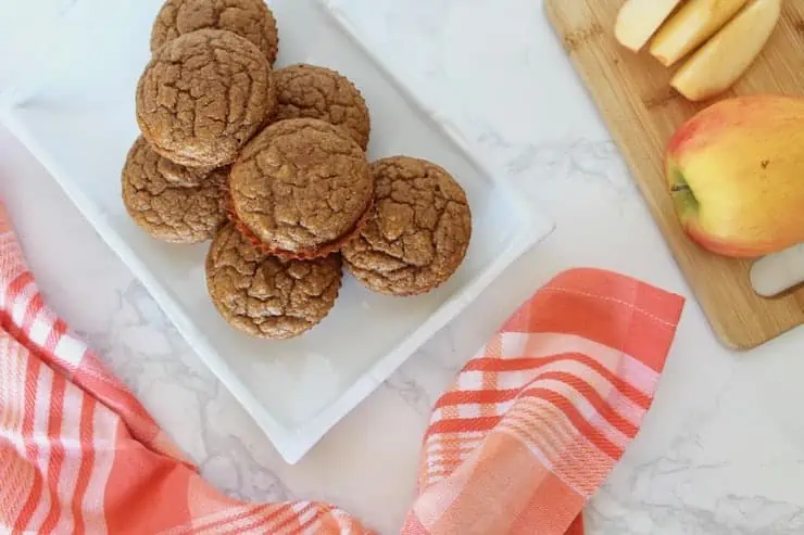 Overhead view of six applesauce muffins on a white plate next to a red and white plaid napkin