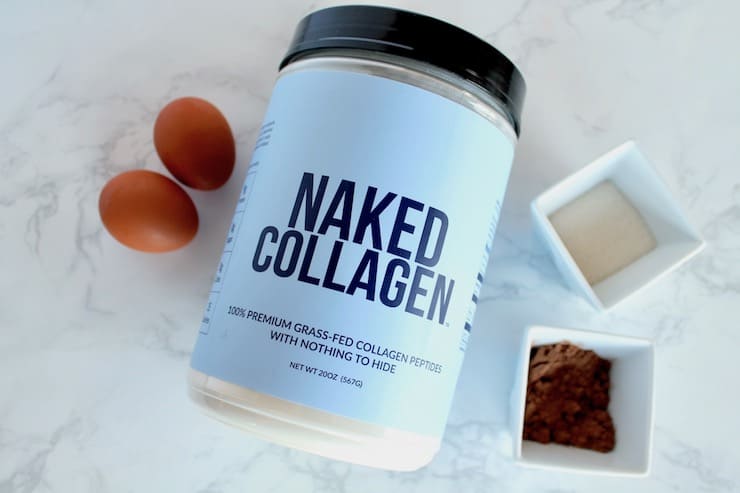 Blue tub of naked collagen next to two eggs and a small bowl of cocoa powder and a small bowl of monk fruit sweetener on a white marble surface
