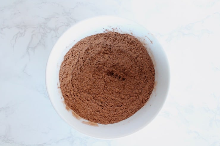 Chocolate keto mug cake mixed dry ingredients in a white bowl on a white marble surface
