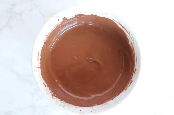 Chocolate keto mug cake mixed batter in a white bowl on a white marble surface