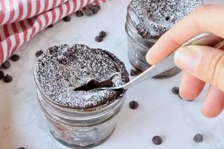 2 small jars with finished chocolate keto mug cake with a spoon in the cake