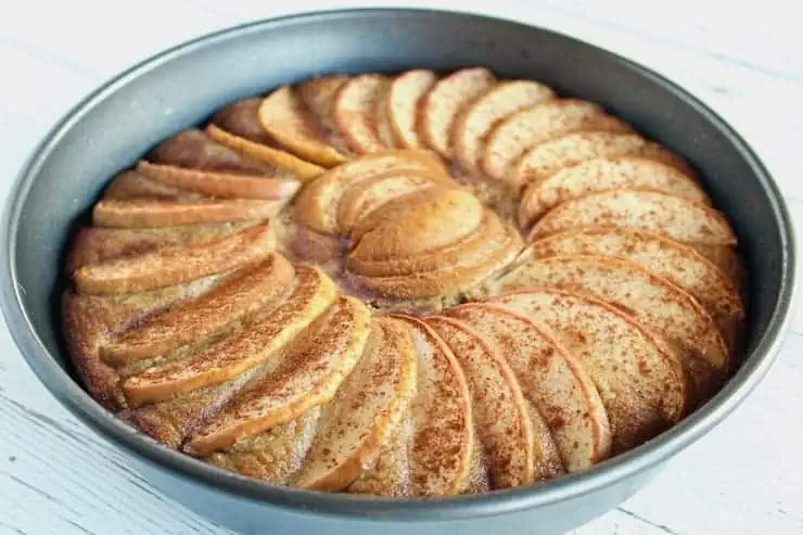 Whole baked apple cake in cake pan on a white wooden table