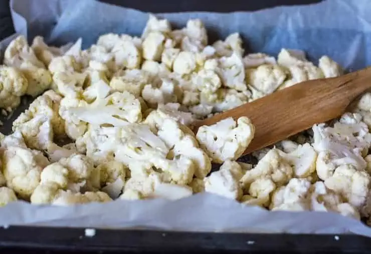 Chopped cauliflower florets on a baking sheet lined with parchment paper with a wooden spatula