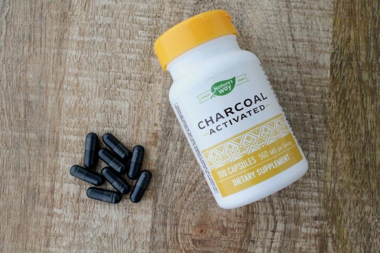 White and yellow supplement bottle of activated charcoal on wooden table next to black capsules of charcoal
