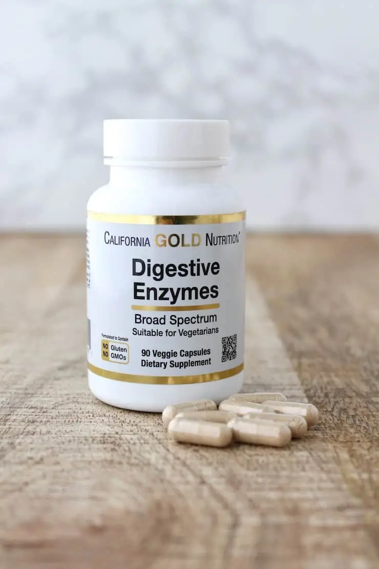 White supplement bottle of digestive enzymes next to capsules on a wooden table
