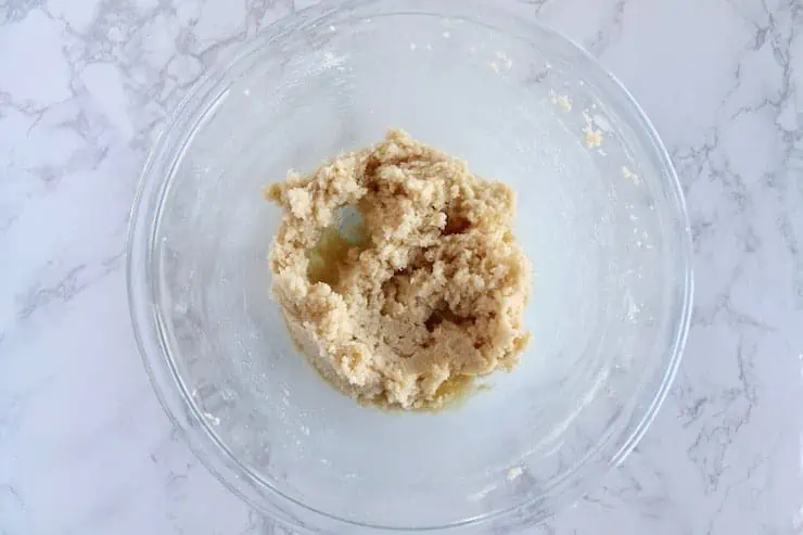 A clear bowl filled with yellow cookie batter on a white marble surface