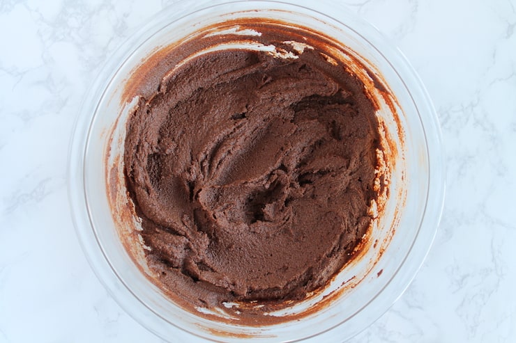 A clear bowl filled with chocolate cookie batter on a white marble surface
