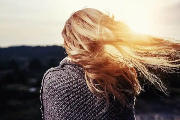 Backside view of a woman's head with her blonde hair blowing in the wind with the sun shinning through