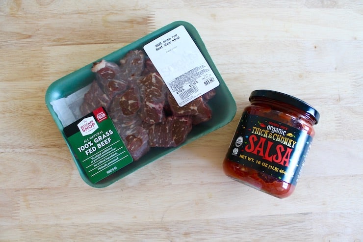 A package of grass fed beef stew meat and a jar of salsa on a wooden table