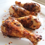 Close up of 4 air fryer chicken drumsticks on white plate with chili flakes sprinkled on them