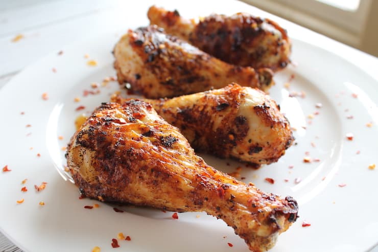 Close up of 4 air fryer chicken drumsticks on white plate with chili flakes sprinkled on them