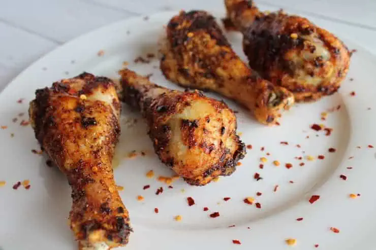 air fryer chicken drumsticks on white plate with chili flakes sprinkled on them