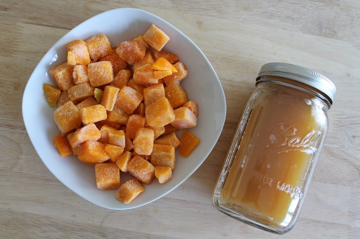 White dish filled with cubed frozen butternut squash next to a jar filled with chicken broth on a wooden table