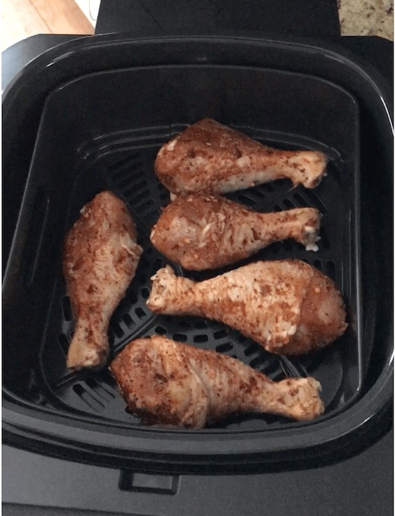 Partially cooked spiced chicken drumsticks in air fryer basket