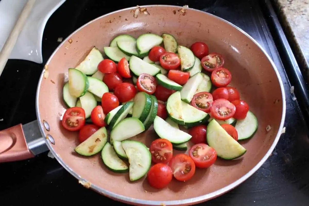 sliced zucchini and tomatoes in a sauté pan on the stove