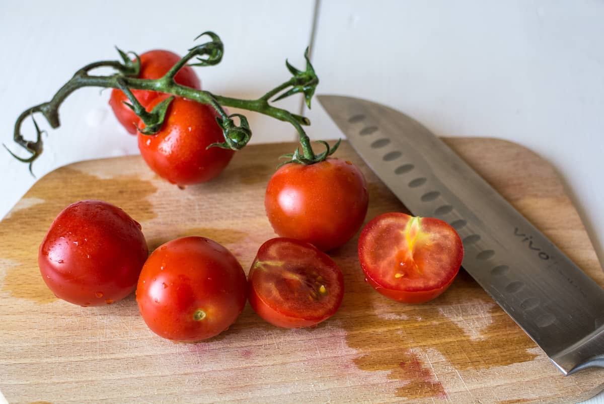 Fresh tomatoes on the vine on a wooden cutting board with a chefs knife on it