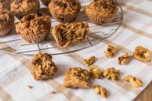 Apple muffin halved on a wire cooling rack next to whole muffins over a white and brown dish towel