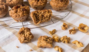 Apple muffin halved on a wire cooling rack next to whole muffins over a white and brown dish towel
