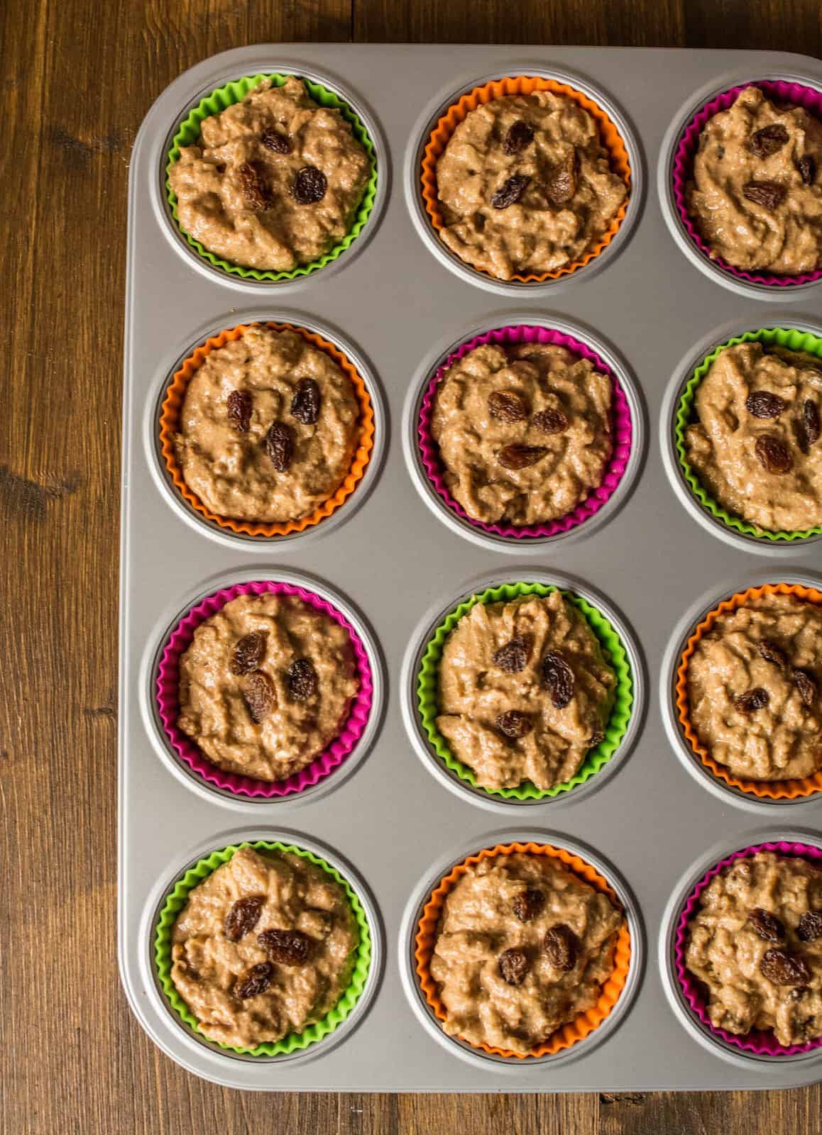 Uncooked apple muffin batter in muffin tin on a brown wooden table