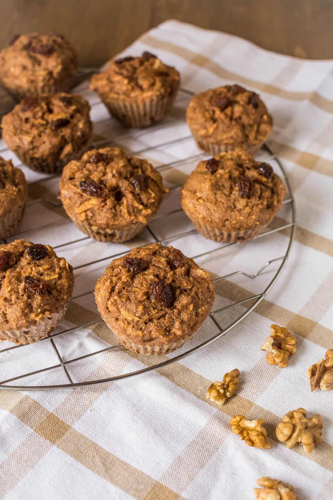 Several gluten free apple muffins on a wire cooling rack over a white and brown dish towel