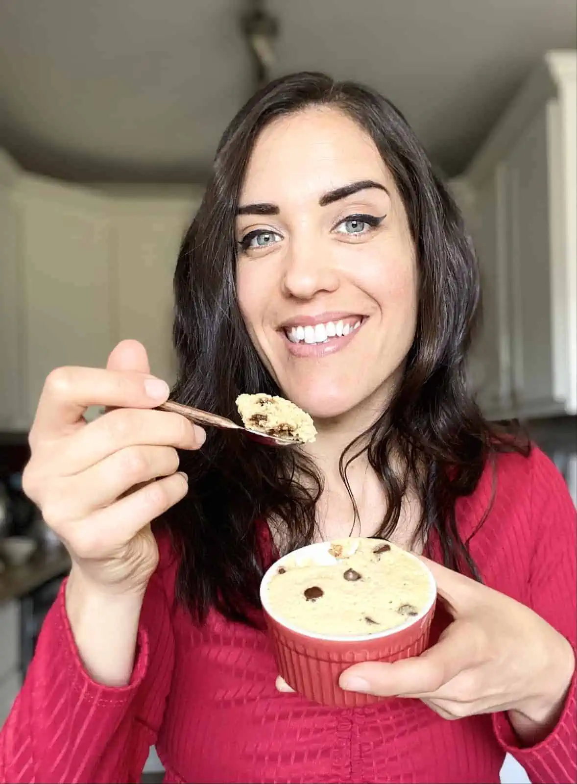 Dark haired woman with red shirt holding mug cake holding up a spoonful of mug cake