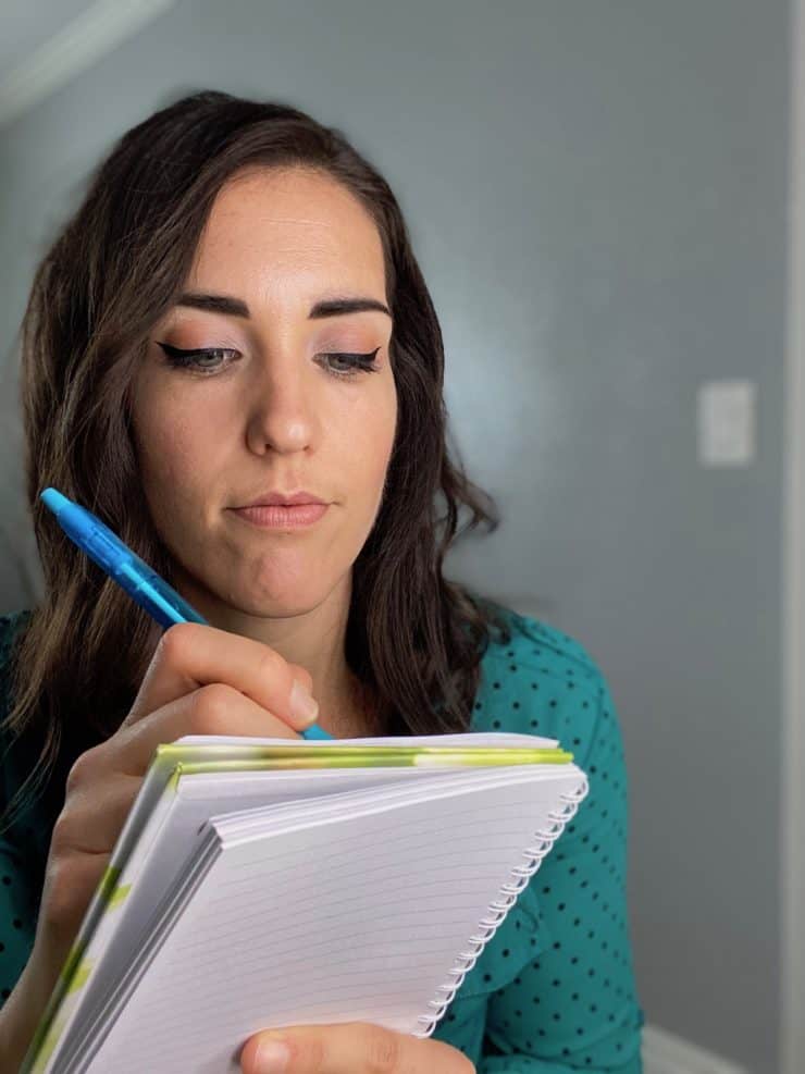 Dark haired woman with green shirt writing in a journal with a pen