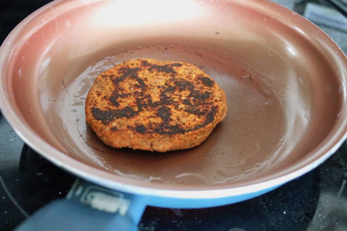 Lentil patty with some black charring on top in an orange skillet