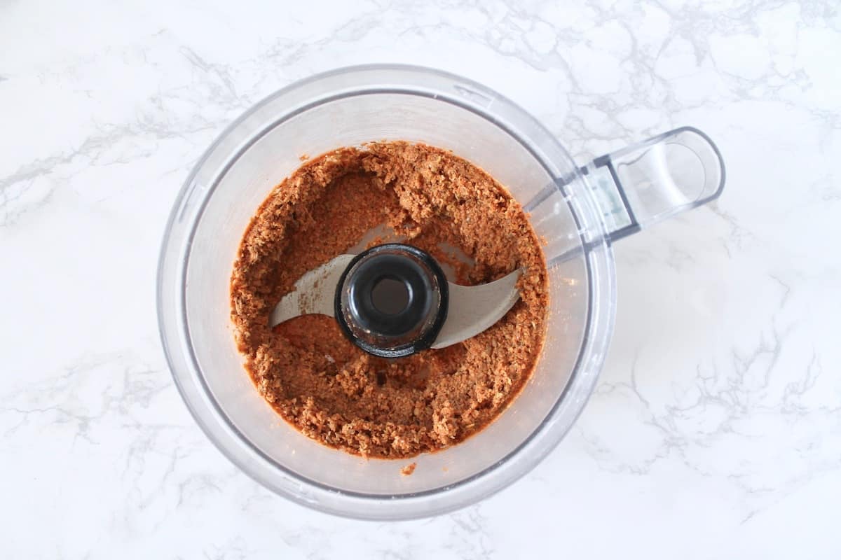 Blended red lentil mixture in a clear food processor on a white marble surface