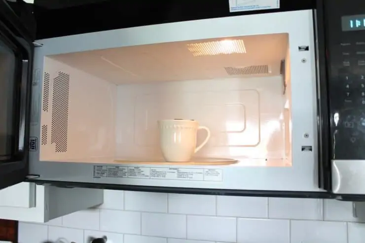 Microwave with an open door with a white mug inside it