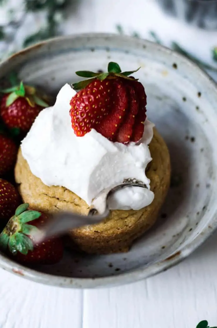 Grey ceramic bowl with yellow cake inside topped with white whipped cream and strawberries