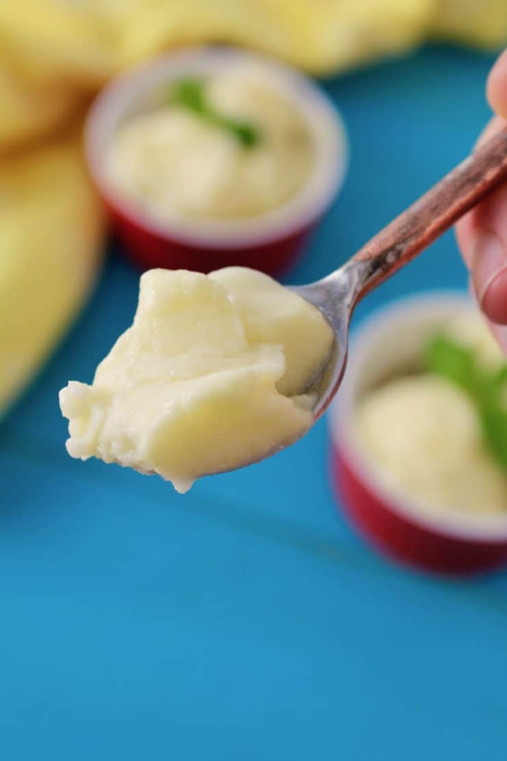 Close up of a spoon with a scoop of pineapple sorbet on it with red ramekins of sorbet on a blue wooden surface in the background