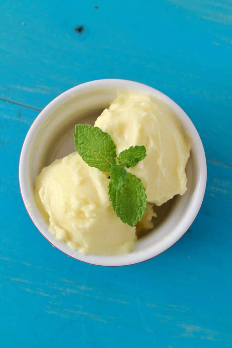 Overhead shot of pineapple sorbet in a white ramekin with mint leaves on top on a blue wooden surface