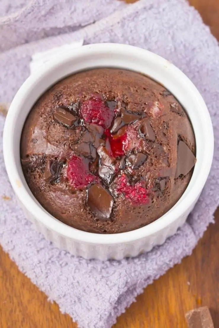 Overhead shot of white ramekin with chocolate cake inside with bits of chocolate and cooked raspberry