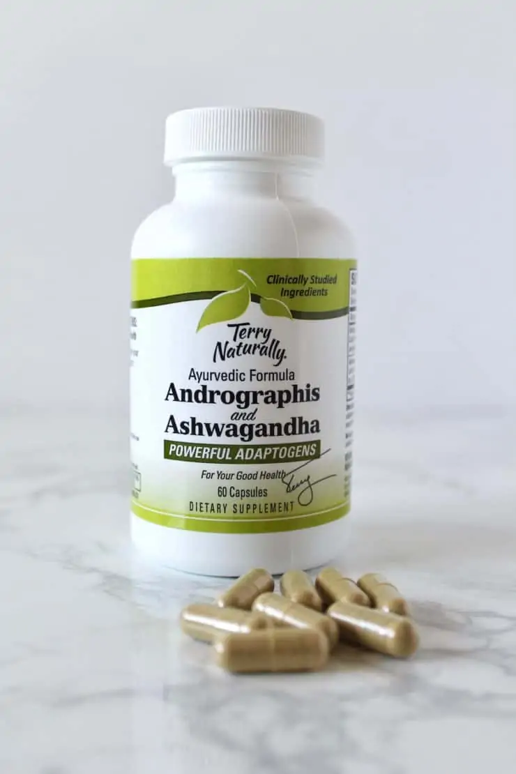 green and white ashwaganda supplement bottle next to loose supplement capsules on a marble surface