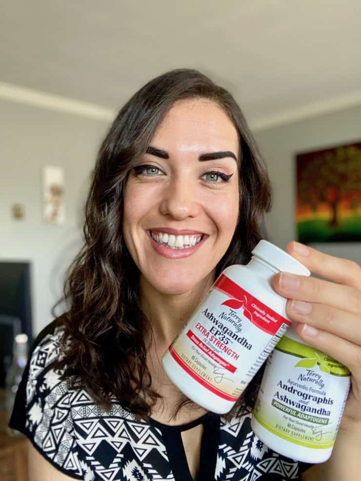 Woman with dark hair smiling holding two ashwaganda supplement bottles