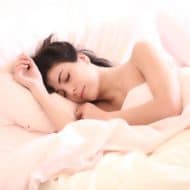 Dark haired woman sleeping in bed with light pink sheets