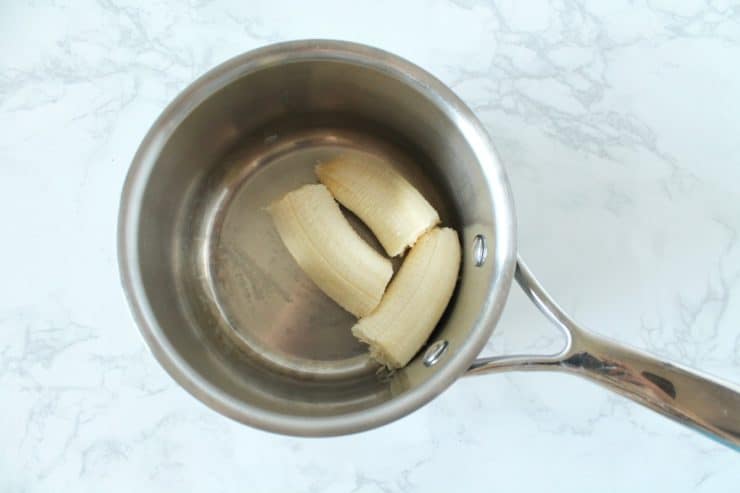 Stainless steel saucepan with broken up banana inside on a white marble surface