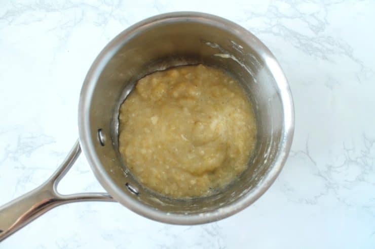 Stainless steel saucepan with mashed up banana inside on a white marble surface