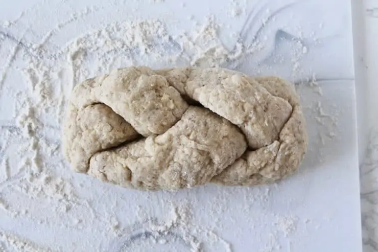 overhead shot of a long loaf of uncooked braided challah on a floured surface
