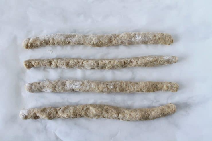four long ropes of challah bread dough in a row on a white surface
