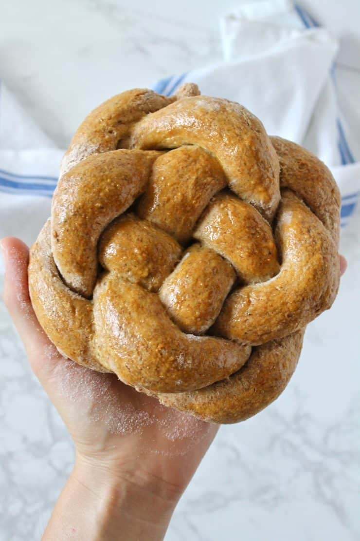 Close up of hand holding a loaf of round braided challah