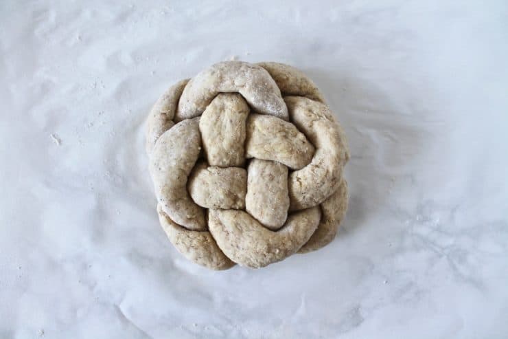 Overhead shot of uncooked round braided challah loaf on a white surface