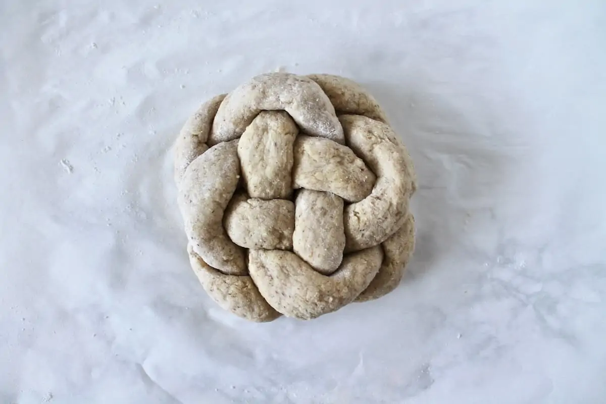 Overhead shot of uncooked round braided challah loaf on a white surface
