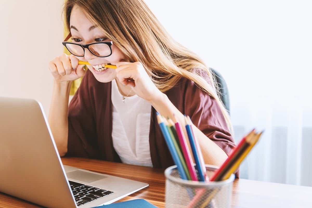 woman biting a pencil sitting at a desk in front of a laptop
