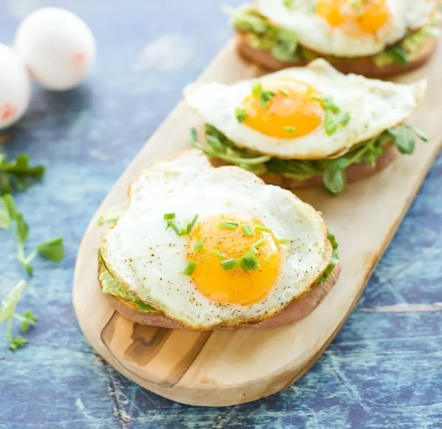 sweet potato toasts with fried egg on top of each one on a long wooden cutting board