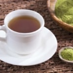white tea cup and saucer with moringa tea in it next to a dish and spoon with green moringa powder in it
